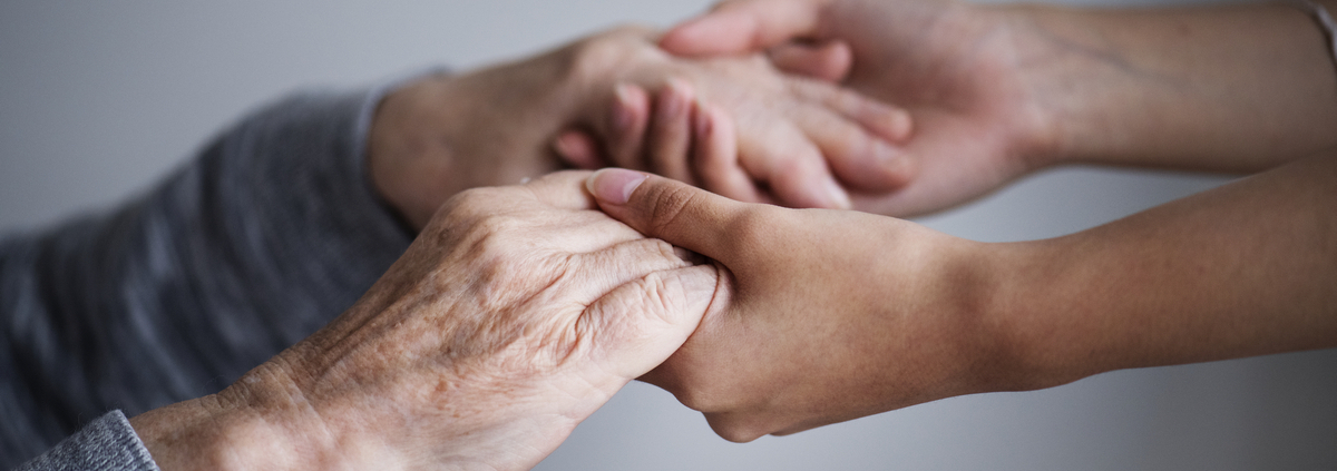 Supporto e assistenza agli anziani: mani di caregiver che tengono quelle di una persona anziana