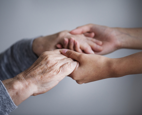 Supporto e assistenza agli anziani: mani di caregiver che tengono quelle di una persona anziana